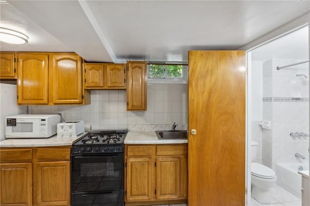 kitchen featuring gas stove, light countertops, white microwave, and a sink
