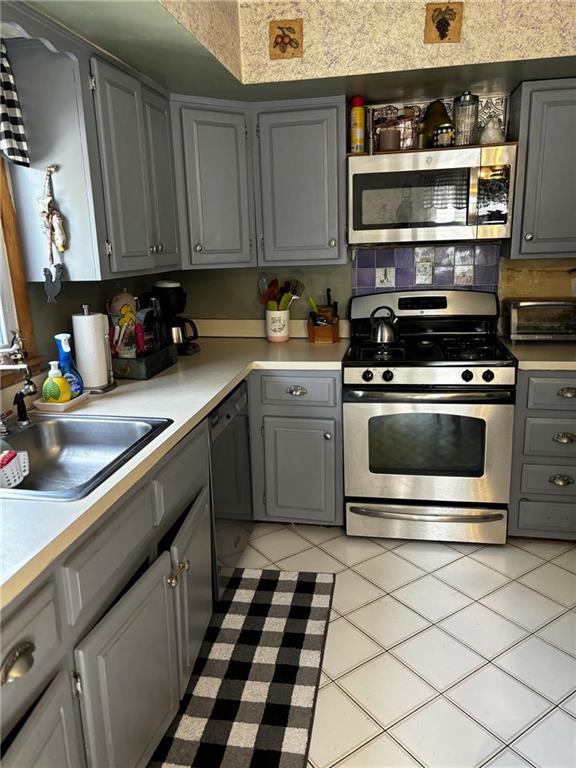 kitchen with light tile patterned floors, sink, appliances with stainless steel finishes, and gray cabinetry