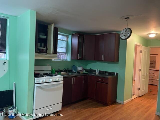 kitchen with light wood-type flooring, dark brown cabinetry, white range with gas cooktop, and sink