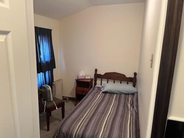 carpeted bedroom featuring vaulted ceiling and radiator