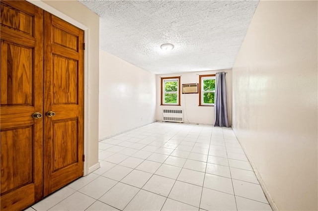 empty room with light tile patterned floors, a textured ceiling, baseboards, a wall mounted AC, and radiator heating unit