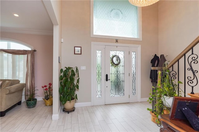 entrance foyer with light hardwood / wood-style floors, a towering ceiling, and crown molding