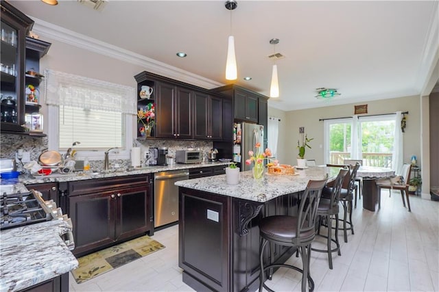 kitchen featuring tasteful backsplash, hanging light fixtures, a center island, stainless steel appliances, and dark brown cabinets