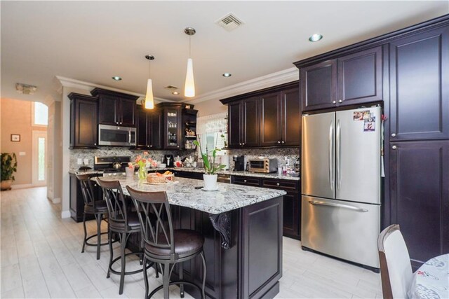 kitchen featuring pendant lighting, a center island, crown molding, light stone counters, and stainless steel appliances