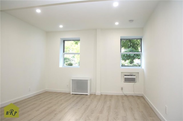 spare room with an AC wall unit, radiator, light wood-type flooring, and plenty of natural light