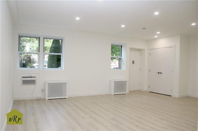 spare room featuring radiator, a wealth of natural light, a wall unit AC, and light hardwood / wood-style floors