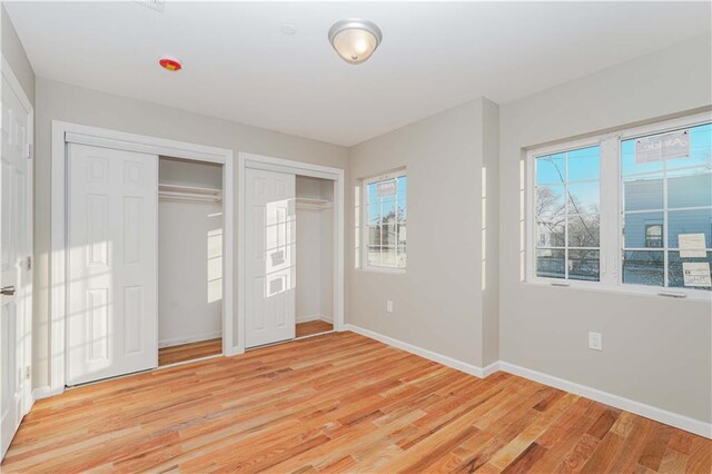 unfurnished bedroom with two closets and light hardwood / wood-style flooring