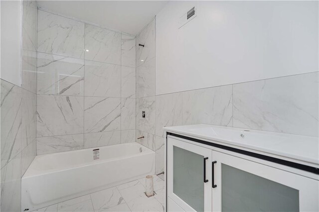 bathroom with tile walls, vanity, and tiled shower / bath