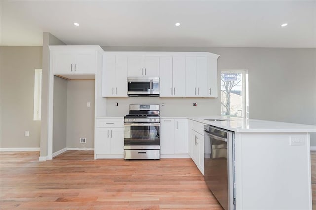 kitchen featuring recessed lighting, appliances with stainless steel finishes, white cabinets, light wood-type flooring, and a peninsula