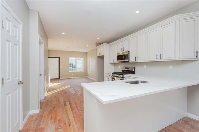 kitchen with stainless steel appliances, white cabinetry, light wood-type flooring, and kitchen peninsula