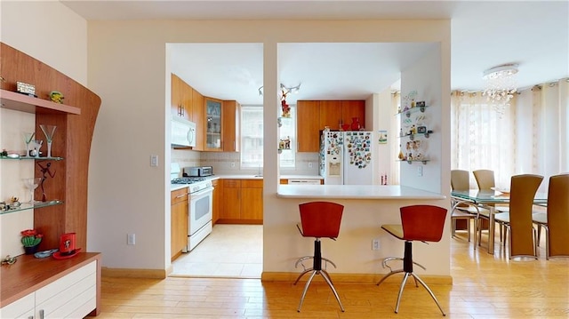 kitchen featuring backsplash, light hardwood / wood-style floors, a breakfast bar, kitchen peninsula, and white appliances