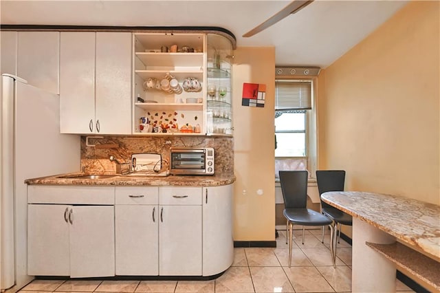 bar with light tile patterned floors, decorative backsplash, light stone counters, and white cabinetry