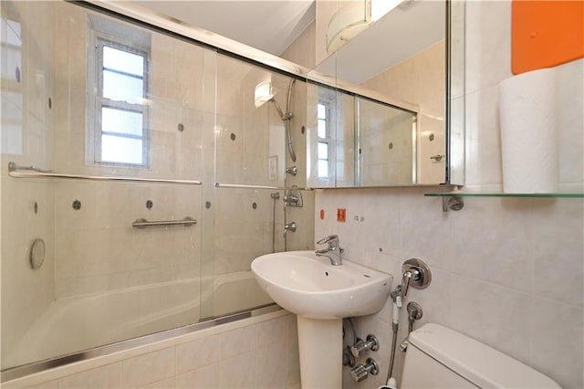 bathroom with toilet, decorative backsplash, tile walls, and shower / bath combination with glass door