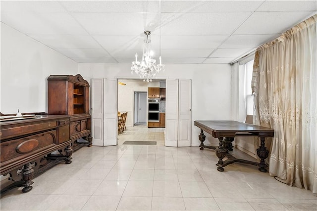 misc room with a notable chandelier, light tile patterned floors, and a paneled ceiling