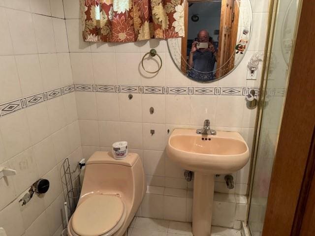 bathroom with tile patterned flooring, toilet, a sink, tile walls, and a stall shower