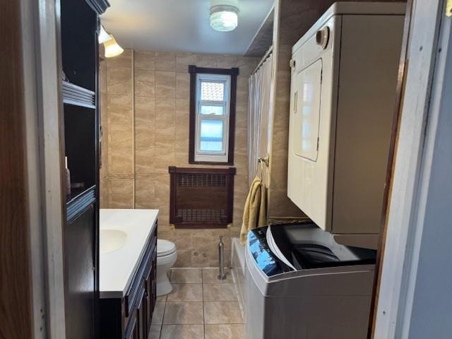 bathroom with stacked washer and dryer, toilet, tile patterned flooring, and vanity