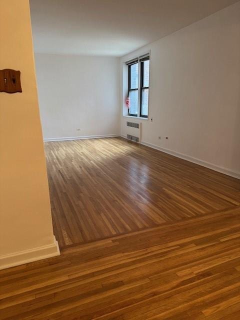 empty room with radiator, baseboards, and wood finished floors