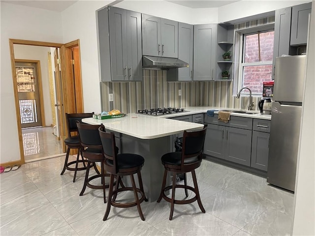 kitchen with stainless steel appliances, decorative backsplash, sink, a kitchen breakfast bar, and gray cabinets