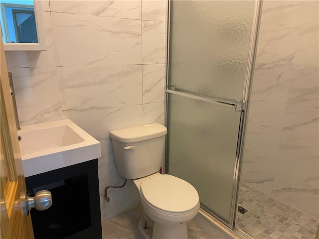 bathroom with tile walls, vanity, a shower with door, and toilet