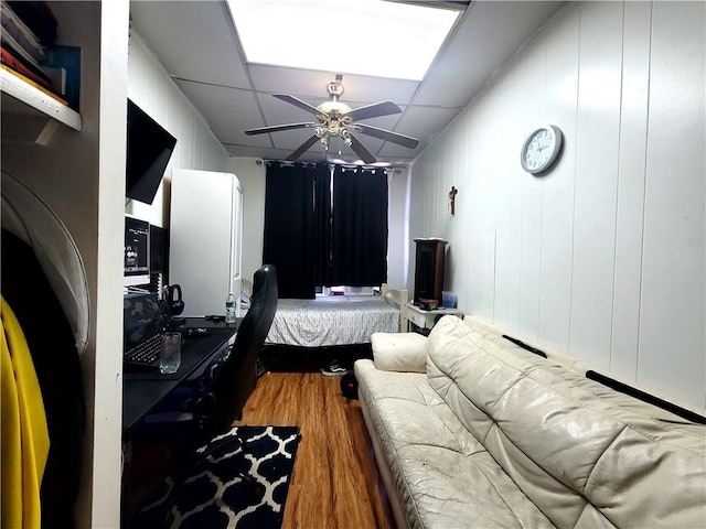 bedroom with a ceiling fan, a drop ceiling, and wood finished floors