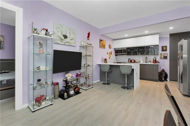 kitchen featuring kitchen peninsula, a kitchen breakfast bar, appliances with stainless steel finishes, light hardwood / wood-style flooring, and white cabinets