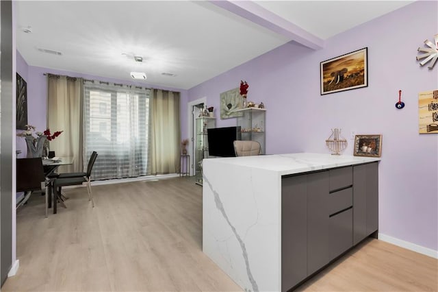 kitchen featuring gray cabinetry, light stone counters, beamed ceiling, kitchen peninsula, and light wood-type flooring