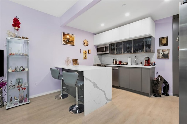 bar with white cabinets, light hardwood / wood-style floors, stainless steel appliances, and gray cabinetry