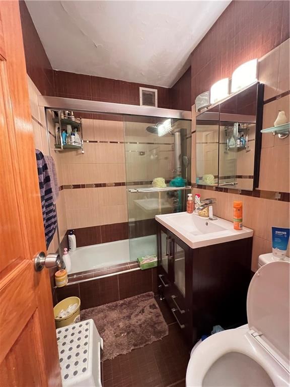 full bathroom featuring bath / shower combo with glass door, tile walls, and toilet