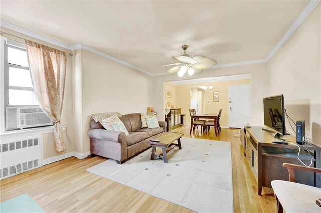 living room with wood-type flooring, radiator heating unit, ceiling fan with notable chandelier, and ornamental molding