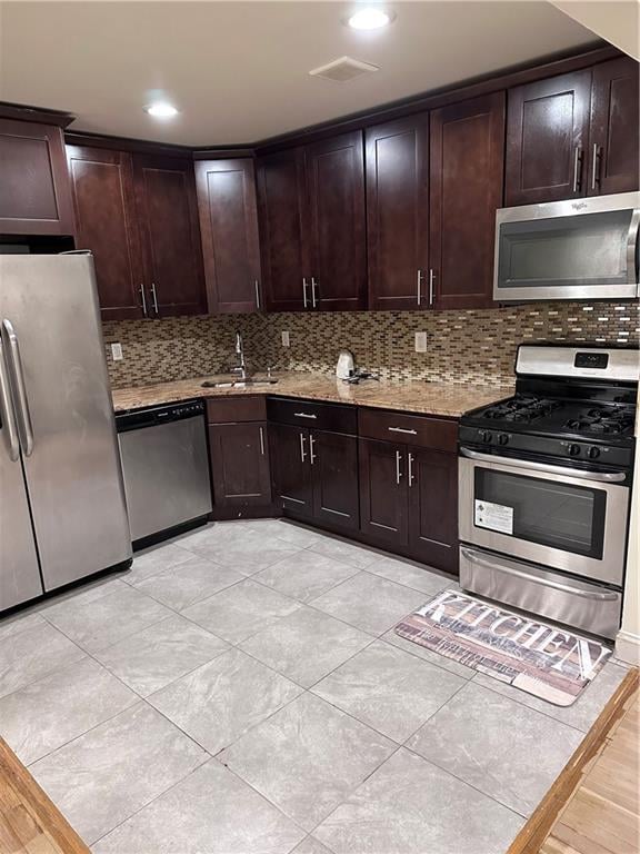 kitchen with dark brown cabinets, light stone countertops, sink, and appliances with stainless steel finishes