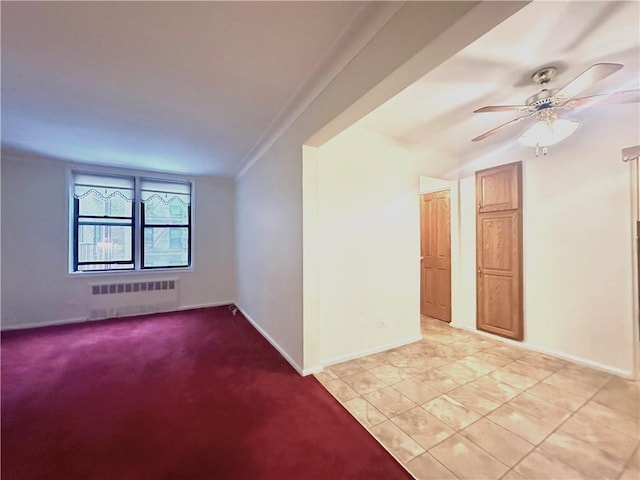 unfurnished room with light colored carpet, radiator heating unit, light tile patterned flooring, ceiling fan, and baseboards