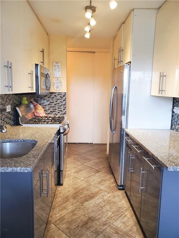 kitchen featuring stainless steel appliances, tasteful backsplash, white cabinetry, a sink, and dark stone counters