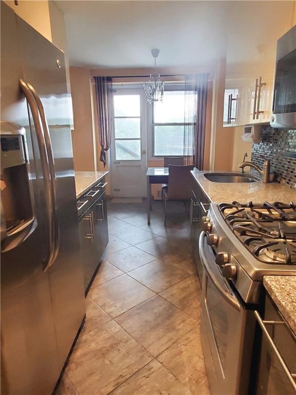 kitchen with light tile patterned floors, decorative backsplash, appliances with stainless steel finishes, a sink, and light stone countertops