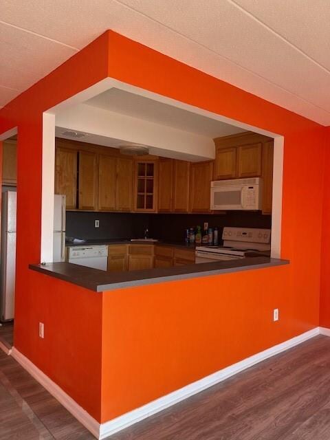 kitchen with dark hardwood / wood-style flooring, sink, white appliances, and kitchen peninsula