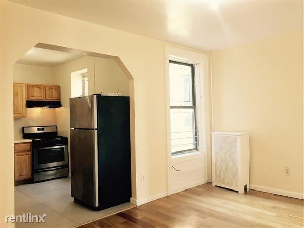 kitchen with appliances with stainless steel finishes, light countertops, light wood-style flooring, baseboards, and under cabinet range hood