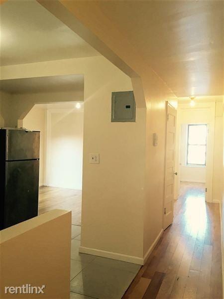hall with light wood-style floors, baseboards, electric panel, and arched walkways