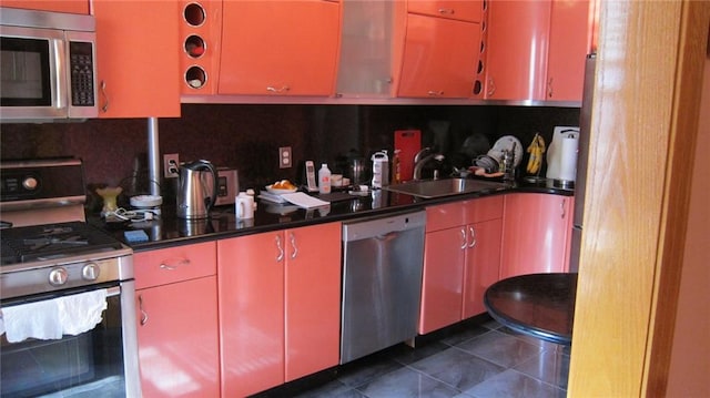 kitchen featuring dark tile patterned floors, a sink, appliances with stainless steel finishes, red cabinets, and backsplash