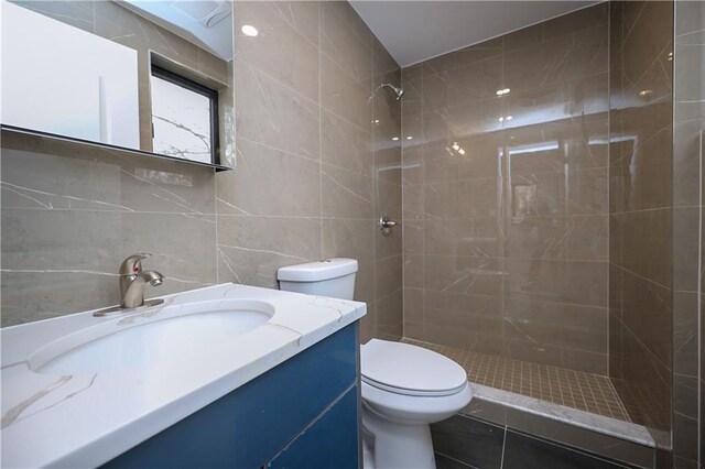 bathroom with a tile shower, vanity, tile walls, and toilet