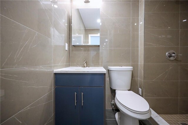 bathroom with vanity, toilet, tile walls, and tiled shower