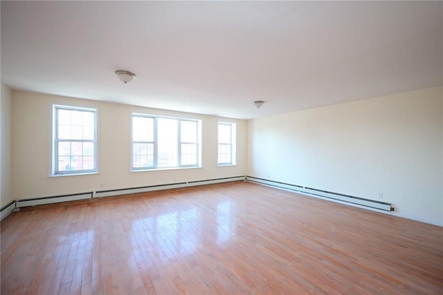 empty room with a healthy amount of sunlight, baseboard heating, and light hardwood / wood-style flooring