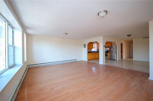 unfurnished living room featuring plenty of natural light, light hardwood / wood-style floors, and baseboard heating