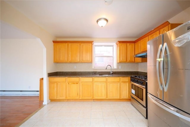 kitchen with sink, stainless steel appliances, a baseboard heating unit, dark stone countertops, and light hardwood / wood-style floors