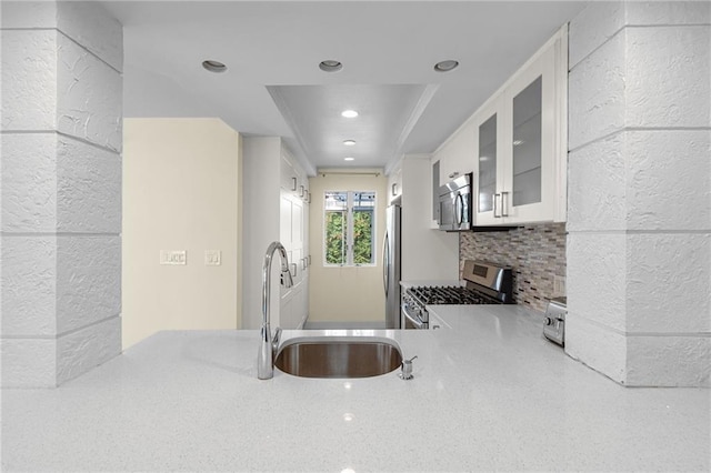 kitchen featuring glass insert cabinets, a sink, stainless steel appliances, white cabinetry, and backsplash