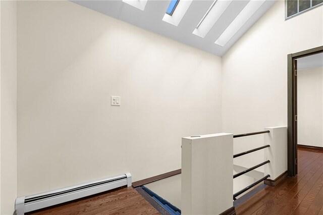 stairs with wood-type flooring, vaulted ceiling with skylight, and baseboard heating