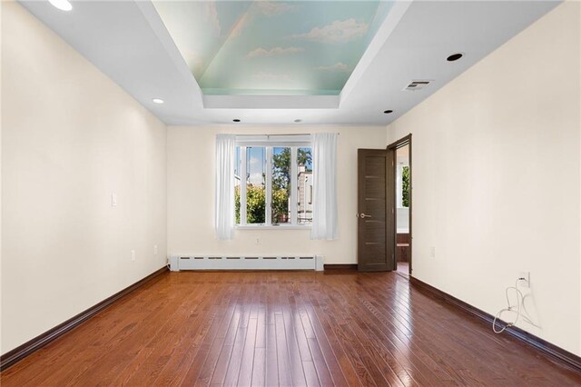 empty room with a baseboard heating unit, dark hardwood / wood-style floors, and a raised ceiling