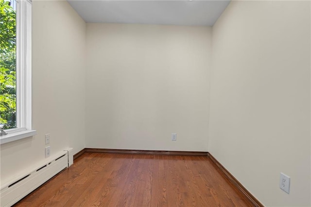 unfurnished room featuring baseboards, a baseboard heating unit, and wood finished floors