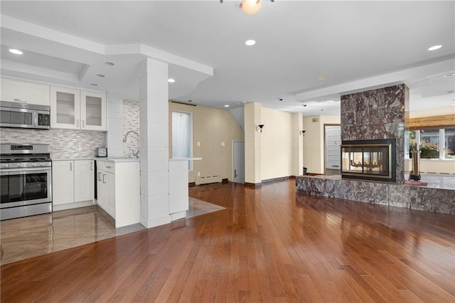 kitchen with appliances with stainless steel finishes, a fireplace, backsplash, white cabinets, and a baseboard heating unit