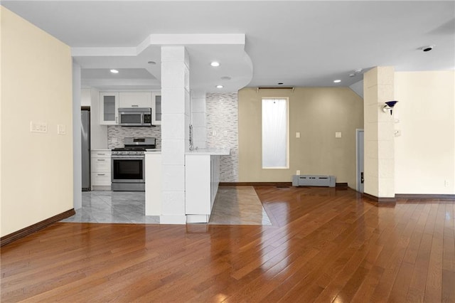 kitchen with appliances with stainless steel finishes, white cabinetry, decorative backsplash, baseboard heating, and light hardwood / wood-style flooring