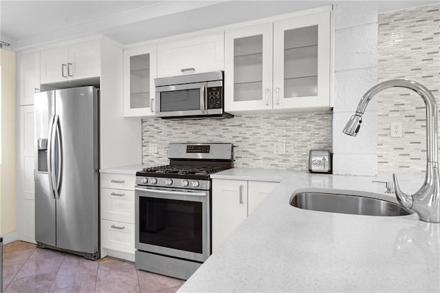 kitchen featuring sink, white cabinetry, light stone counters, appliances with stainless steel finishes, and backsplash