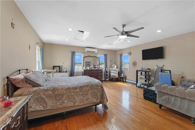 bedroom with ceiling fan, a skylight, a wall unit AC, and light wood-type flooring